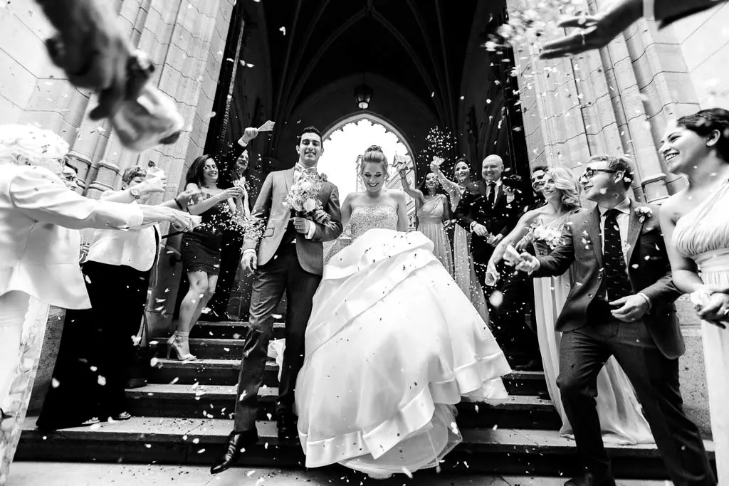 Sortie d'un couple de jeune marié descendant les marches de l'église, sous les confettis des convives