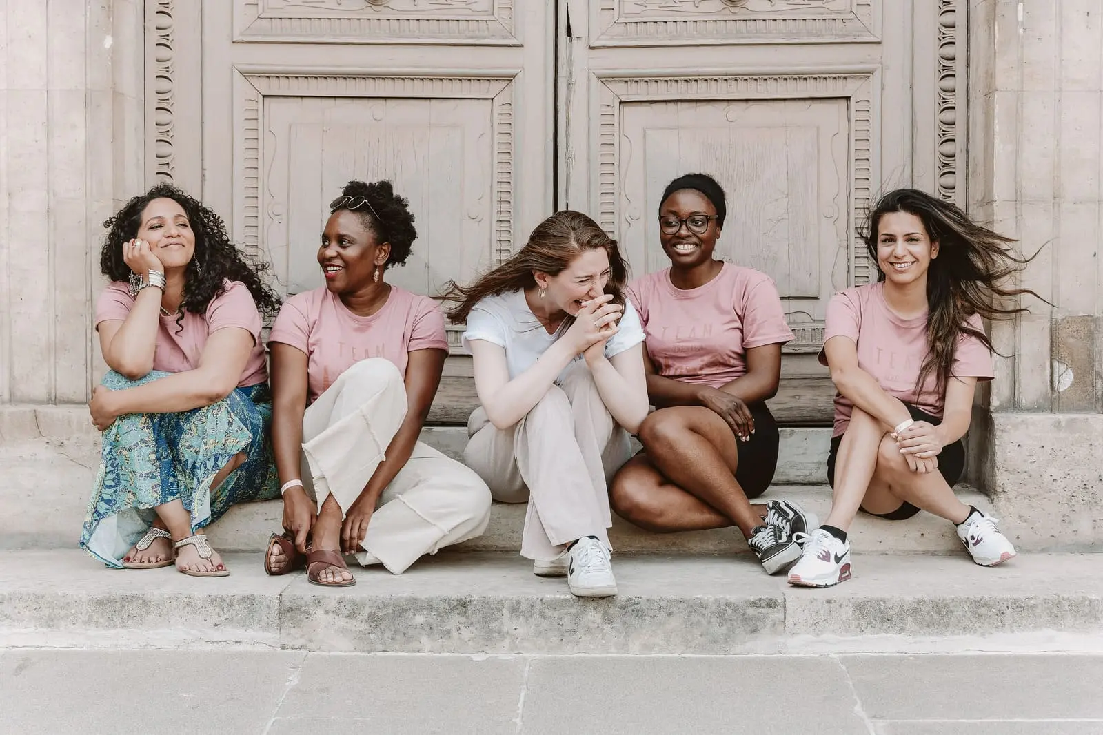Un groupe de filles est assise sur les marches au Louvre et plaisantent pendant la séance photo