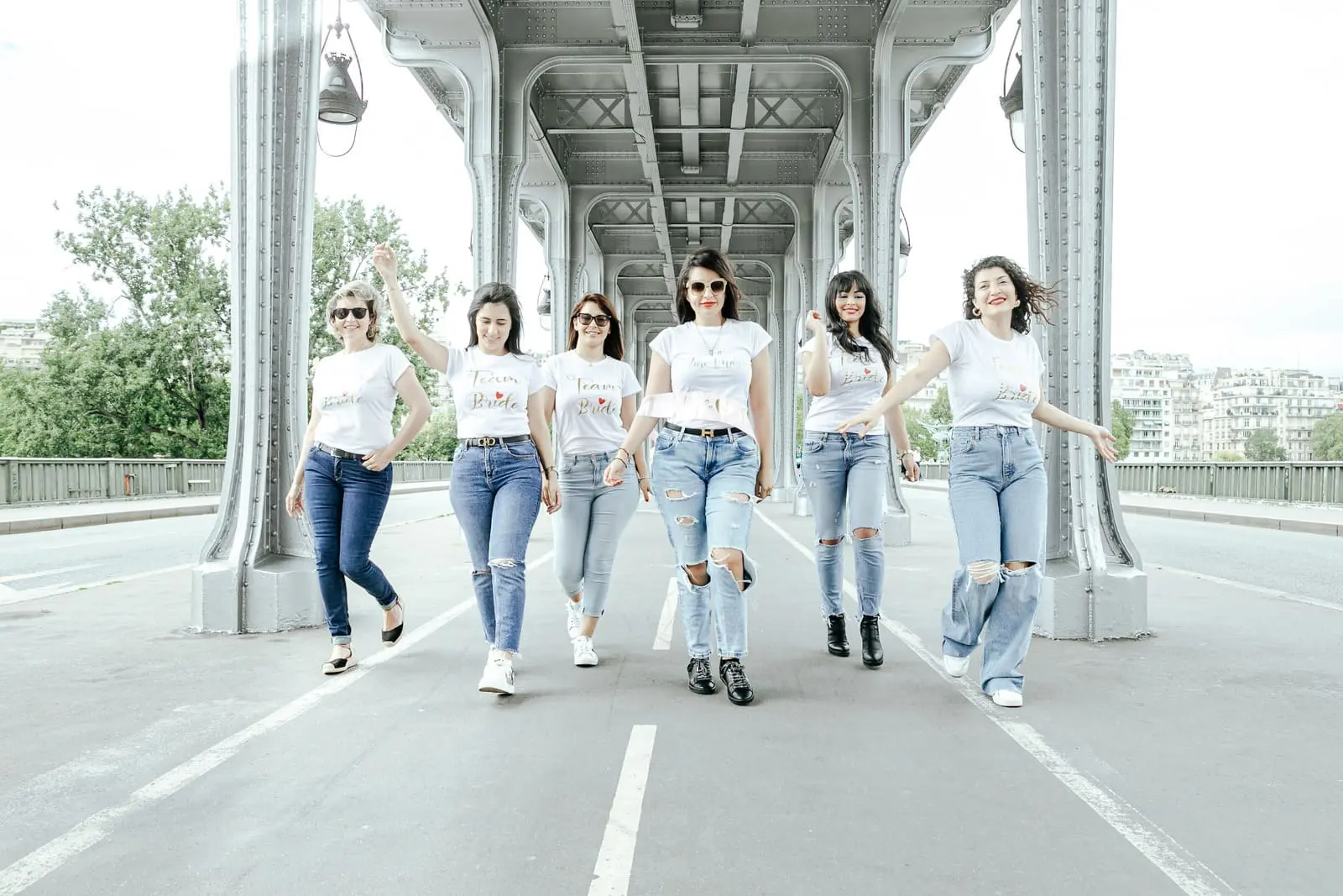 Un groupe de 6 filles défilent, en jean et t-shirt blanc Team Bride sur le pont Bir Hakeim lors d'un séance photo EVJF.