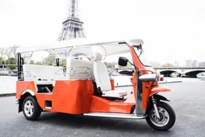 Photographie d'un tuktuk rouge aux pieds de la Tour Eiffel