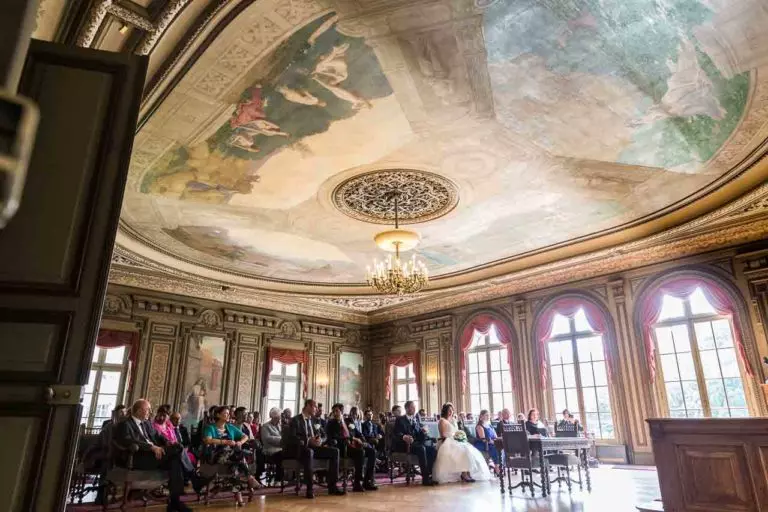 Photographie des mariés et de leur convives, dans la salle des mariages d'une mairie à Paris, pendant la lecture des articles du code civil