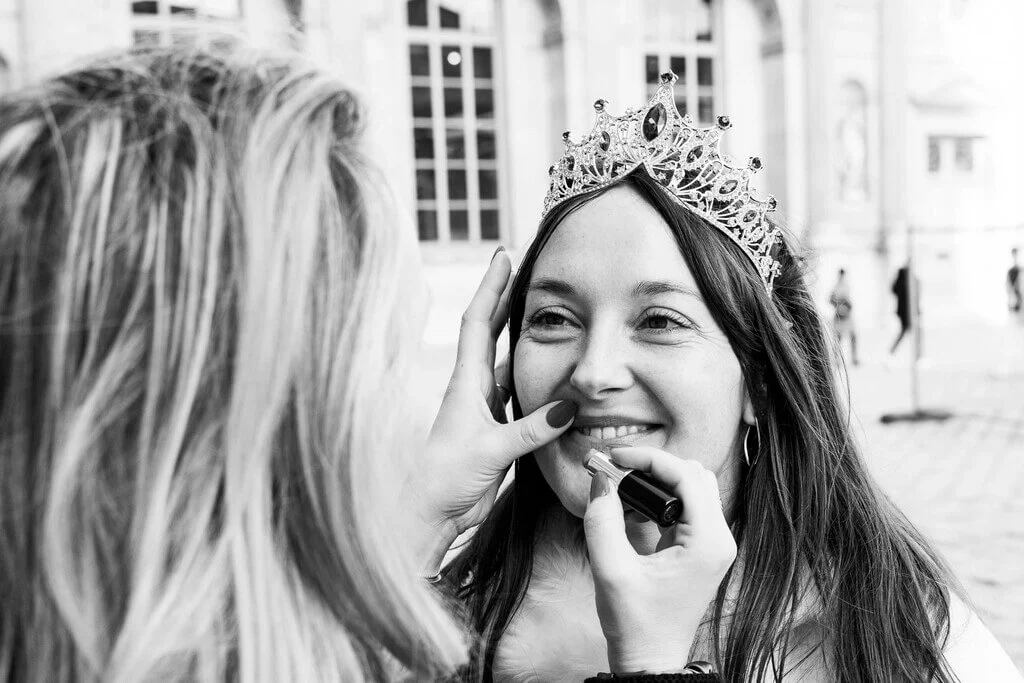 Une demoiselle d'honneur applique du rouge à lèvres à la future mariée qui porte un diadème sur la tête. Photo réalisé pendant un shooting EVJF